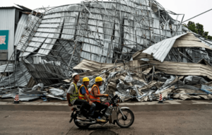 People drive past a crumpled building after a tornado hit Guangzhou